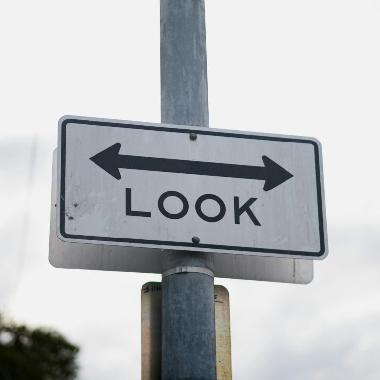 weißes Schild an einem Laternenpfahl, darauf ein Pfeil, der sowohl nach links als auch nach rechts zeit, darunter das Wort "look"